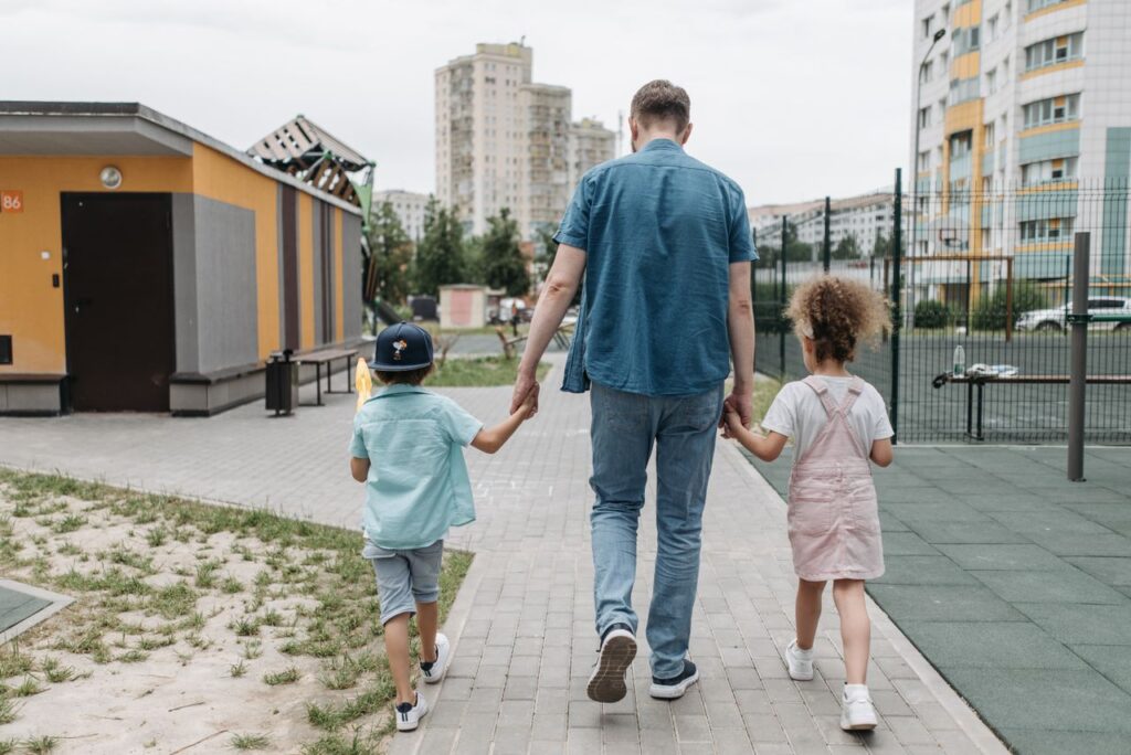 Father and children holding hands, walking on an urban sidewalk in daylight.